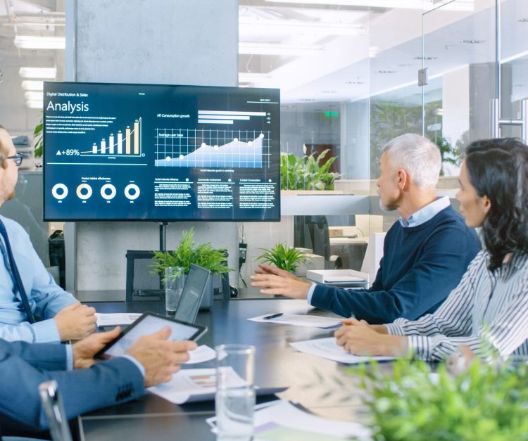 Board of Directors Has Annual Meeting, Diverse Group of Business People in the Modern Conference Room Discuss Statistics and Work Results. In the Background Projector Showing Company Growth. Board of Directors Has Annual Meeting, Diverse Group of Business People in the Modern Conference Room Discuss Statistics and Work Results. In the Background Projector Showing Company Growth.